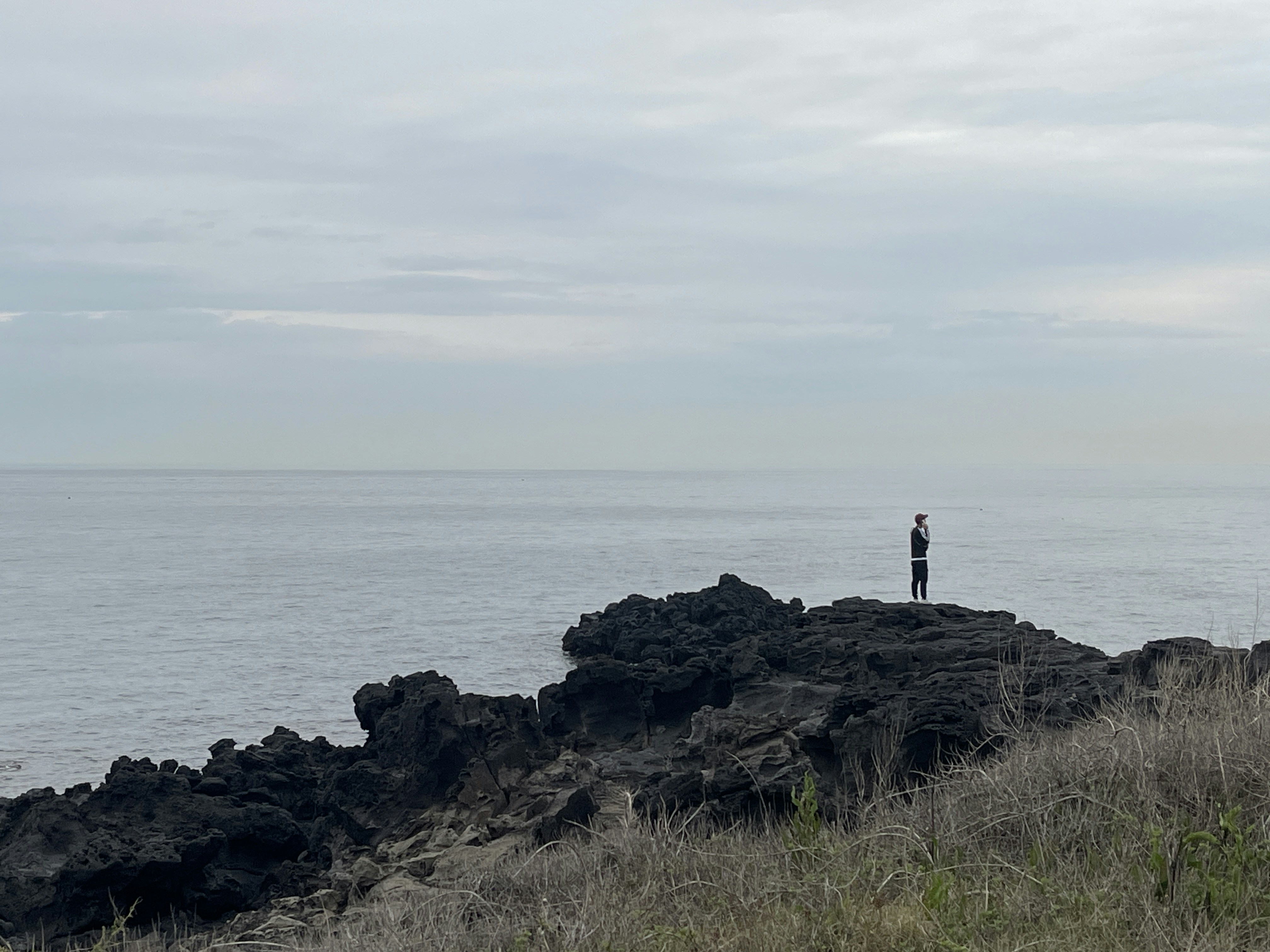 a man standing on top of a rocky cliff next to the ocean