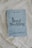 A book titled 'Royal Wedding' by Marina Minelli rests on an ornate white lace fabric. The book has a light blue cover with elegant floral patterns and bold black text. At the bottom, there is a subtitle in Italian.
