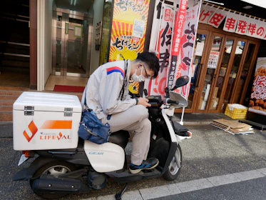 A smiling motoboy checking earnings on a smartphone while sitting on his motorcycle.