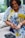 A person is preparing to check their blood sugar using a glucometer. They hold a lancet in one hand while gently pressing the other. The background is softly out of focus, lending a sense of calm to the setting. The person is wearing a vibrant, patterned blue and yellow shirt.