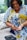 A person is preparing to check their blood sugar using a glucometer. They hold a lancet in one hand while gently pressing the other. The background is softly out of focus, lending a sense of calm to the setting. The person is wearing a vibrant, patterned blue and yellow shirt.