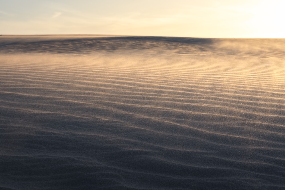 the sun is setting over a sand dune