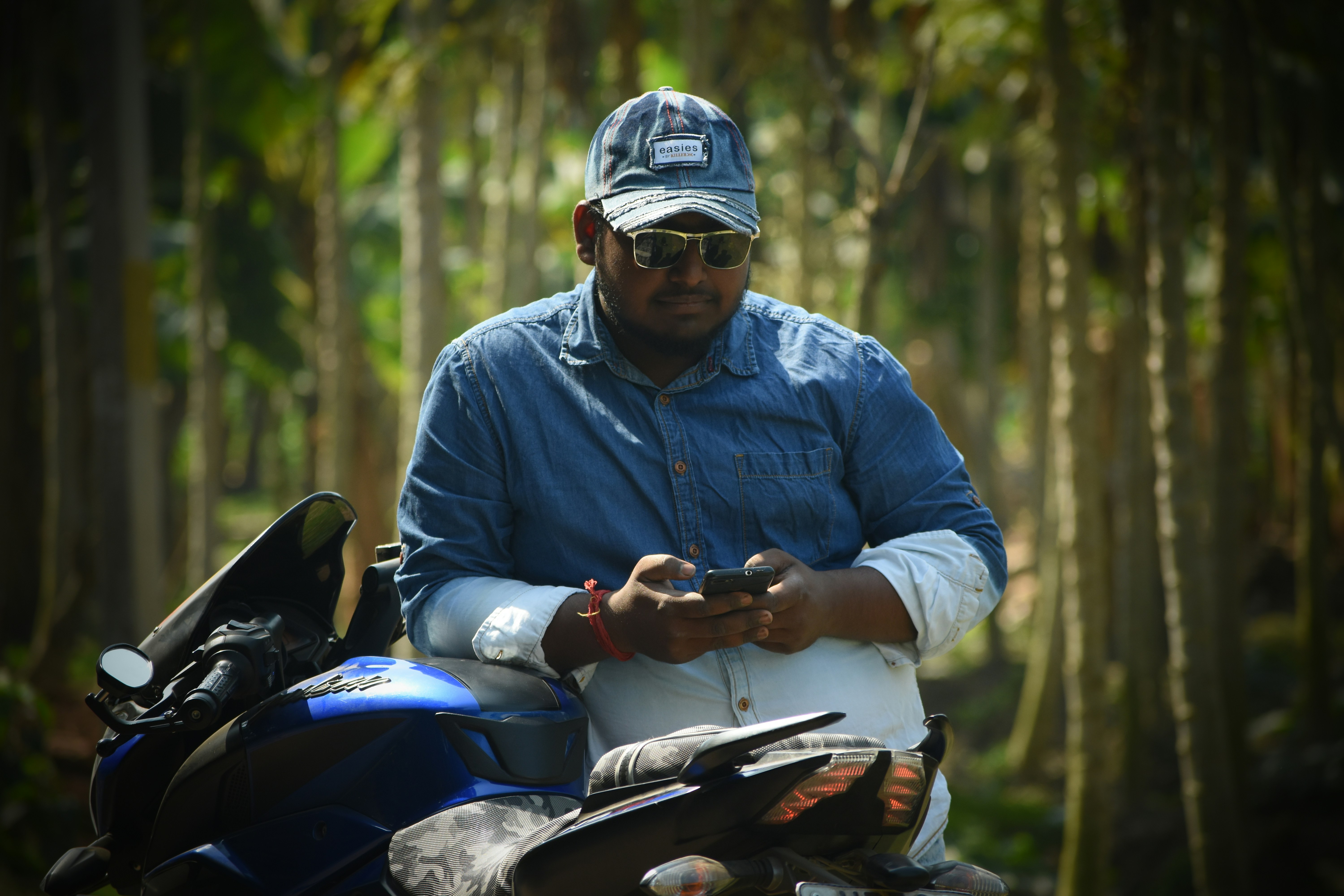 A group of Goan motorcycle pilots, some older, some younger, standing in a circle, engaged in a serious discussion, looking worried. A few are holding their helmets.