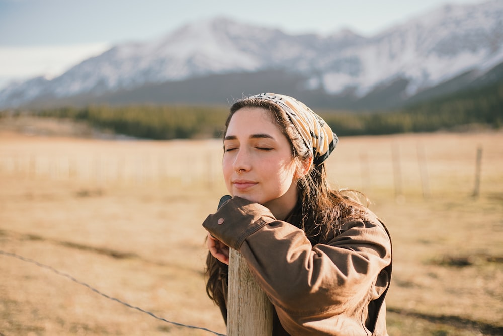 a woman leaning on a fence with a mountain in the background