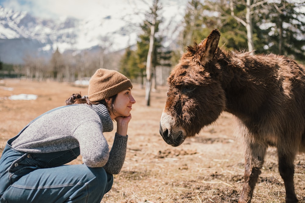 a woman kneeling down next to a donkey