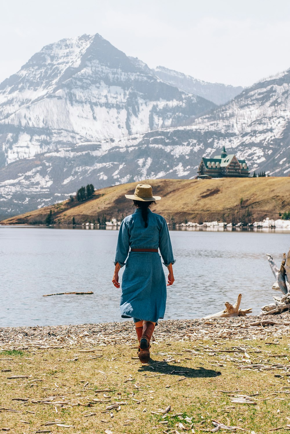 Una donna in un vestito blu e cappello che cammina da un lago