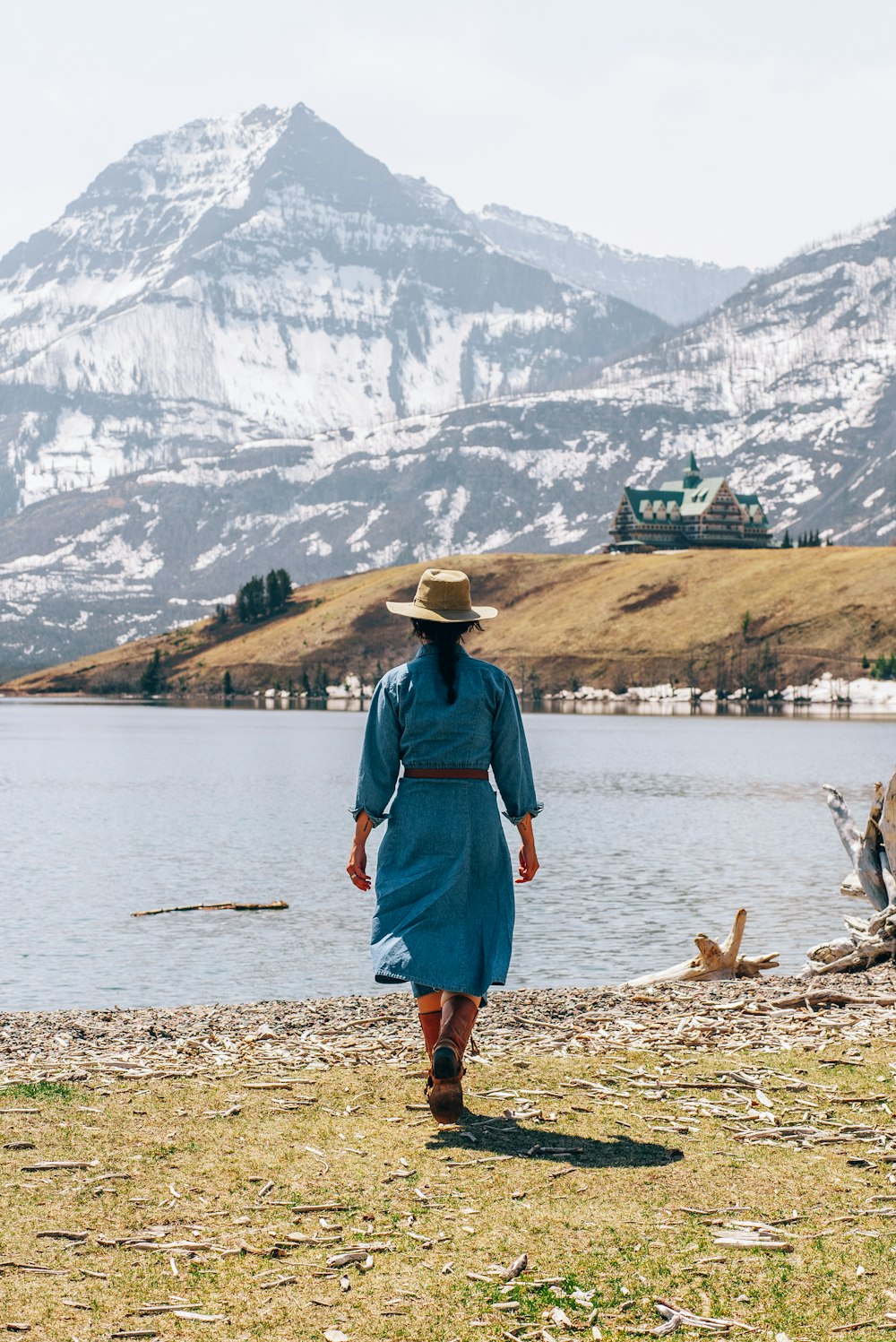 a woman in a blue dress and hat walking by a lake