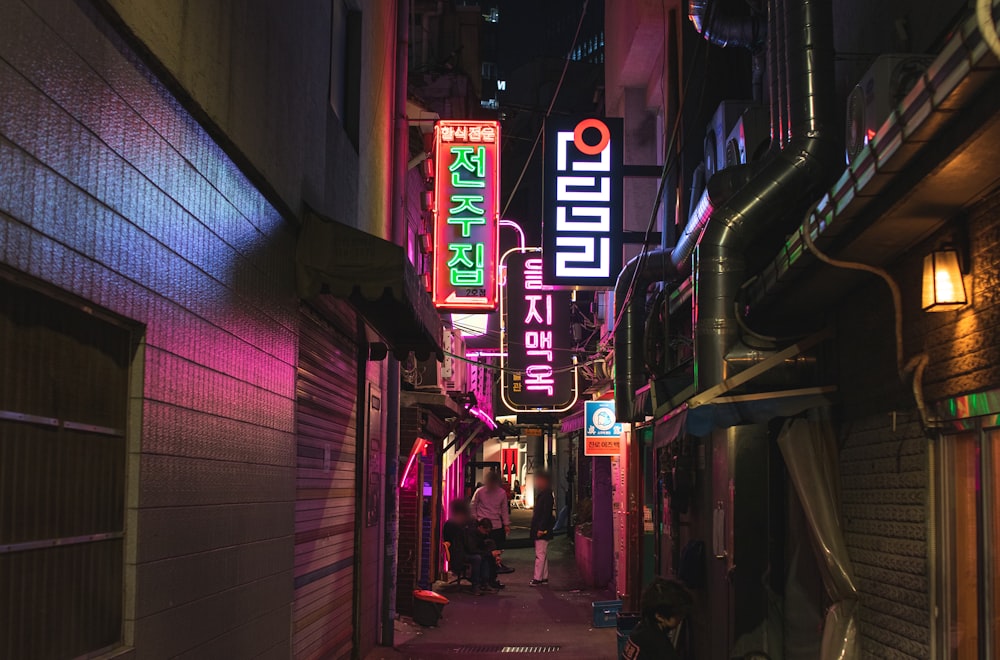 a narrow alley way with neon signs on the buildings