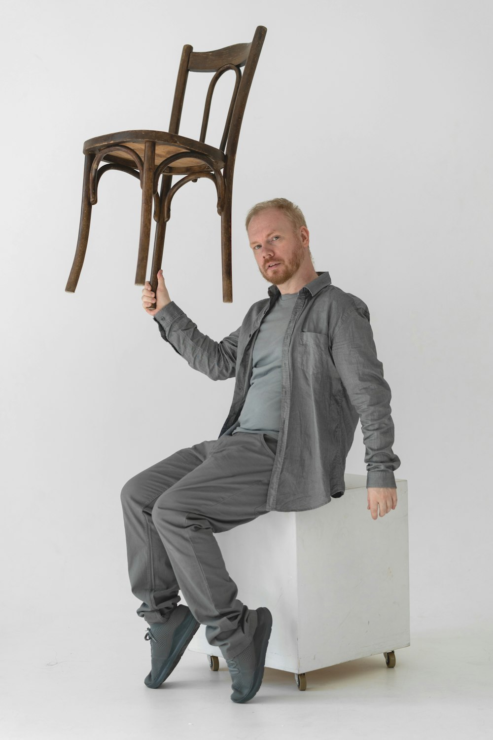 a man sitting on a stool holding up a chair