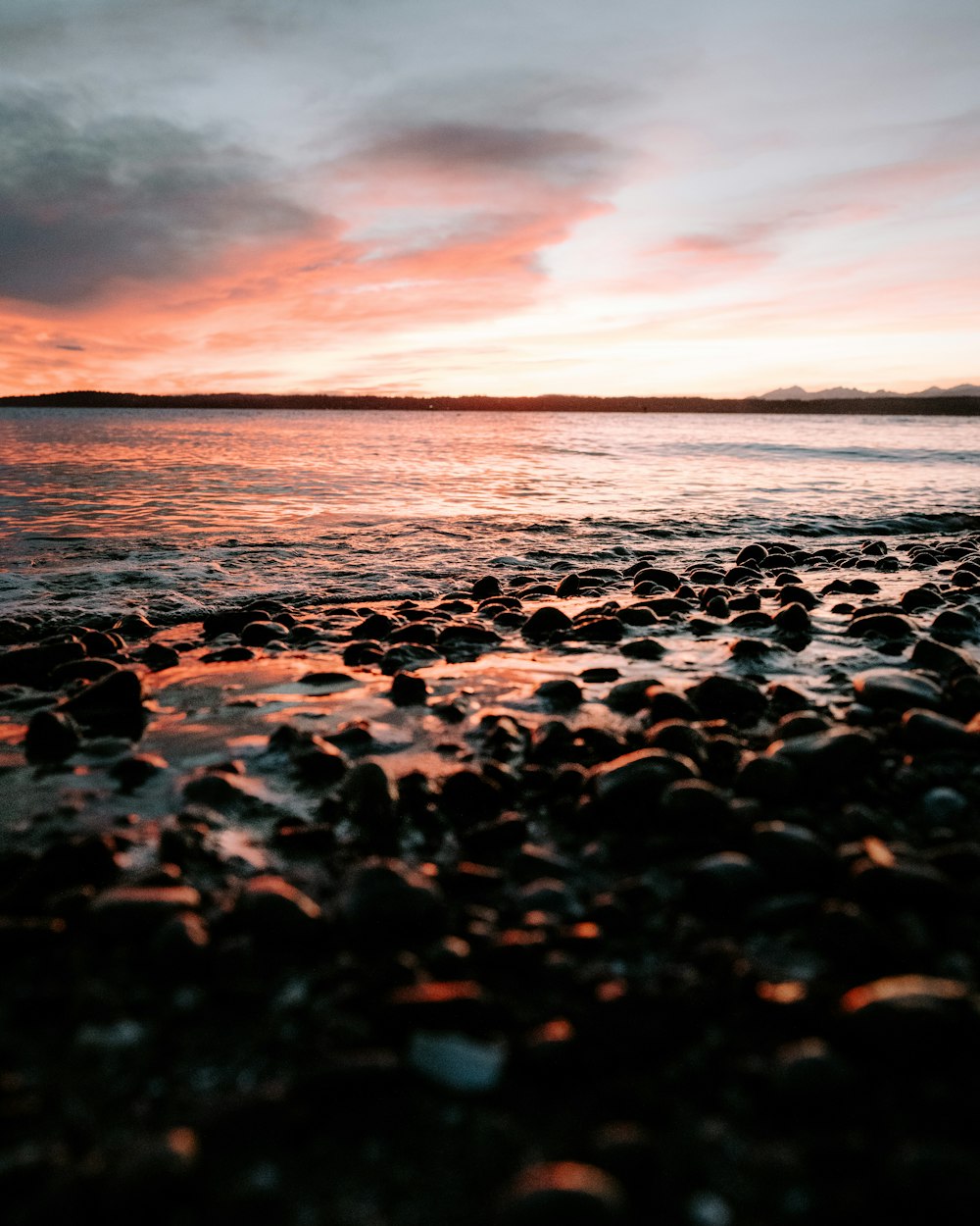 the sun is setting over the ocean with rocks in the foreground