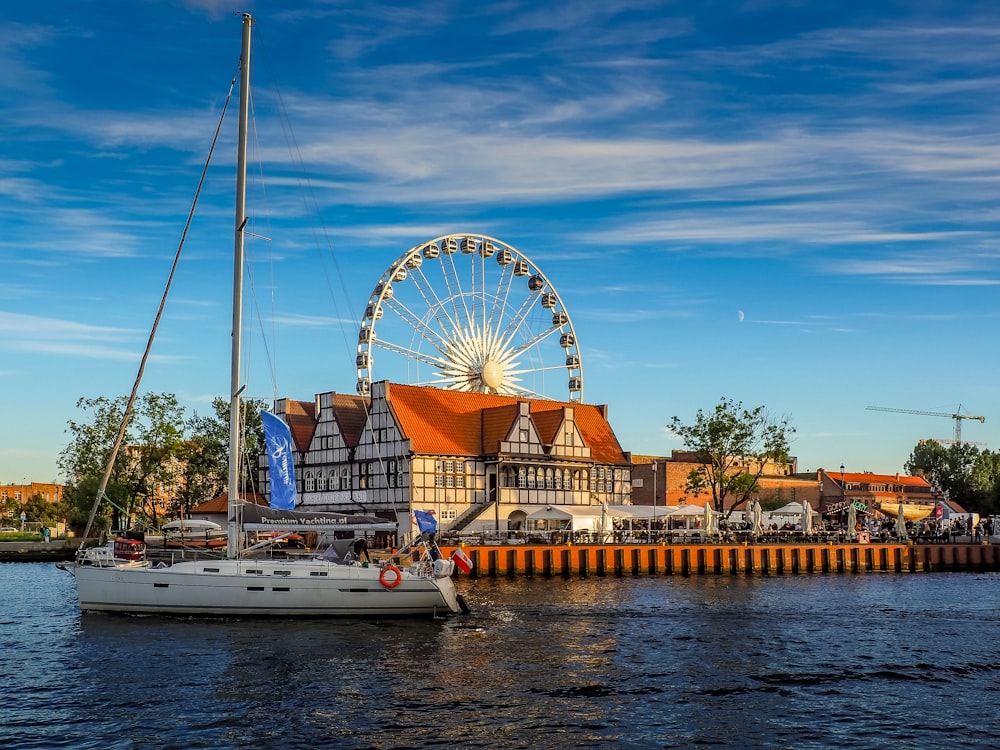 a sailboat in the water next to a building with a ferris wheel in the
