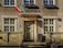 The entrance of a building with two flags, one Polish and one Ukrainian, hanging next to the word 'BIBLIOTEKA' above the door. The building features ornate, carved stonework around the door and windows.