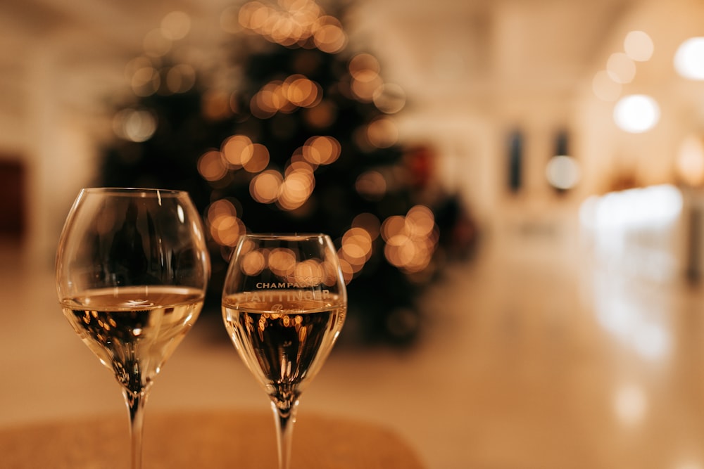 two glasses of wine sitting on a table in front of a christmas tree