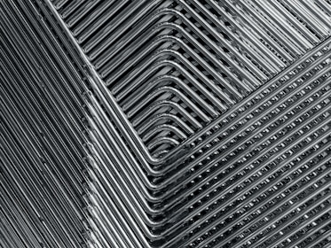 A close-up view of stacked metal chairs, showcasing a geometric pattern formed by the overlapping chair legs and seats. The metallic texture is prominent, highlighting the sleek, streamlined appearance of the arrangement.