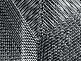 A close-up view of stacked metal chairs, showcasing a geometric pattern formed by the overlapping chair legs and seats. The metallic texture is prominent, highlighting the sleek, streamlined appearance of the arrangement.