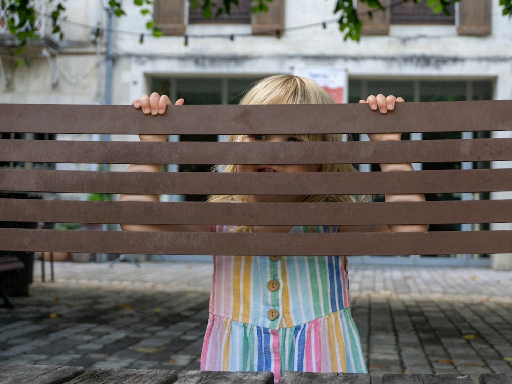 a little girl hiding behind a wooden bench