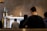 A religious ceremony is taking place with people kneeling in prayer before an altar. The altar is adorned with ornate candlesticks, a golden monstrance, chalices, and floral decorations. Soft lighting casts a reverential atmosphere over the setting.