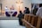 People are gathered inside a church, participating in a religious service. Two clergy members stand at the altar, which is decorated with a purple cloth and a display of wheat. Congregants are seated or kneeling in wooden pews, facing the altar. A crucifix is mounted on the wall behind the altar.