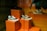 A display of three sneakers is arranged on orange pedestals inside a store. The shoes are a mix of black, white, and teal, with white laces, and they are positioned at different heights. Part of a person's leg and hand, possibly belonging to a mannequin, is visible in the upper right corner, suggesting a retail environment.