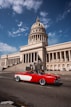 a red and white car driving past a large building