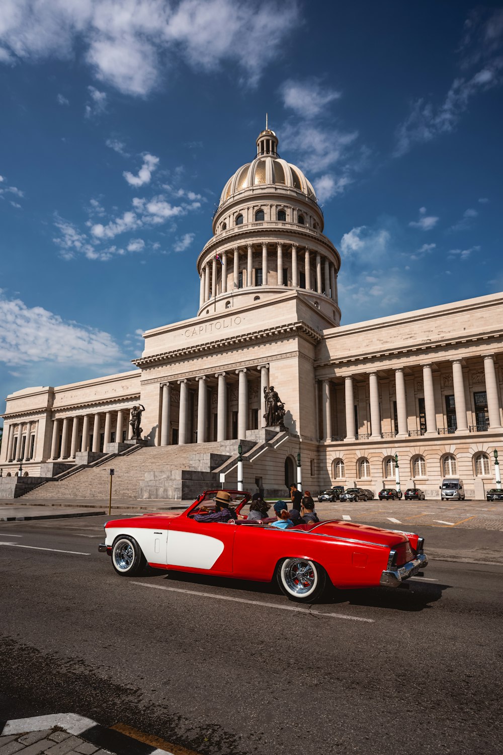 a red and white car driving past a large building