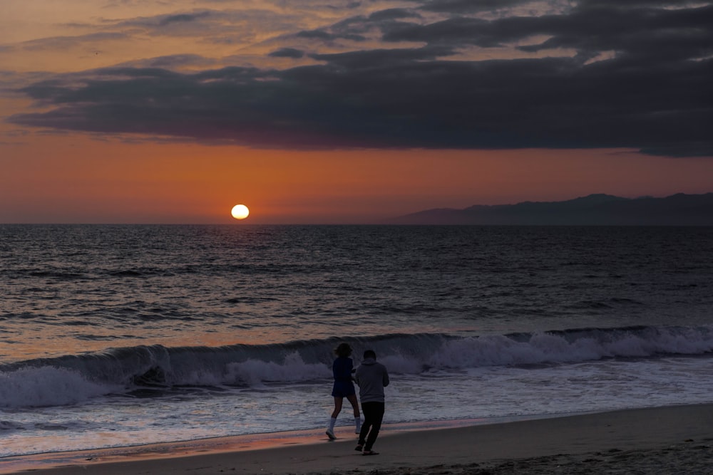 um par de pessoas em pé em cima de uma praia de areia