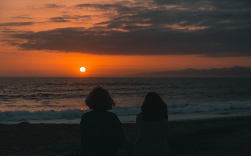 Zwei Personen, die an einem Strand sitzen und den Sonnenuntergang beobachten