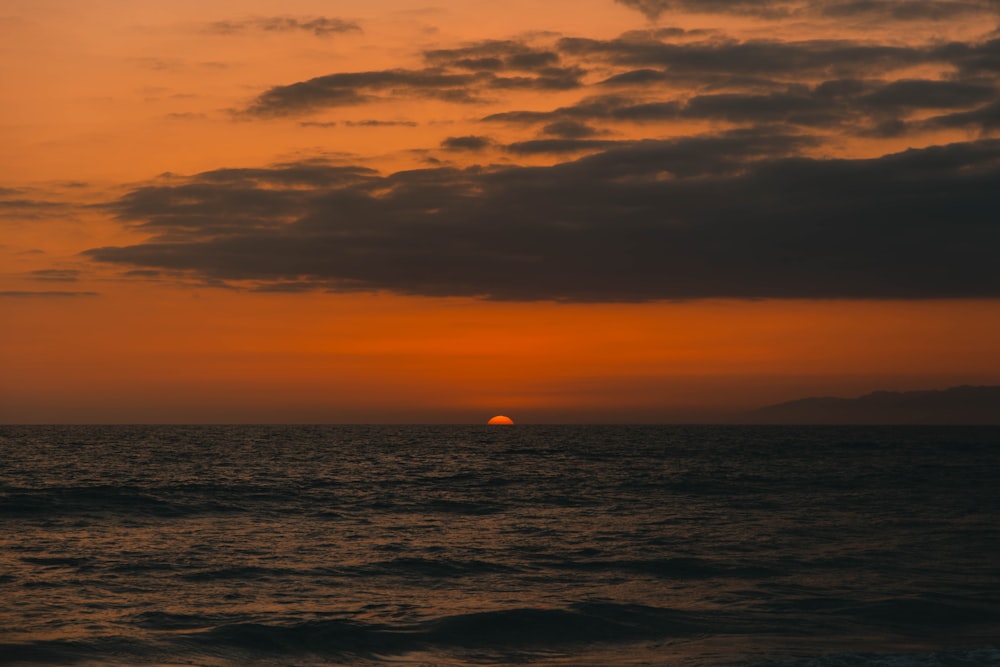 um pôr do sol sobre o oceano com um barco ao longe