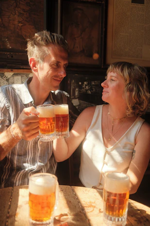 Couple sharing a laugh over craft beers in a cozy, sunlit brewery corner with green and charcoal accents.