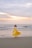 A joyful woman wearing a bright, flowing beach dress standing by the ocean at sunset.