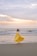 A joyful woman wearing a bright, flowing beach dress standing by the ocean at sunset.