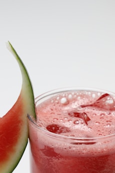 a glass of watermelon juice next to a slice of watermelon