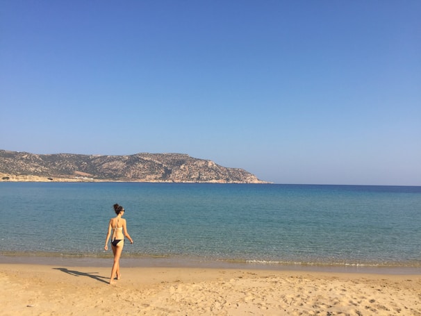 Model walking along the shore wearing a clean, elegant one-piece swimsuit in soft pastel.