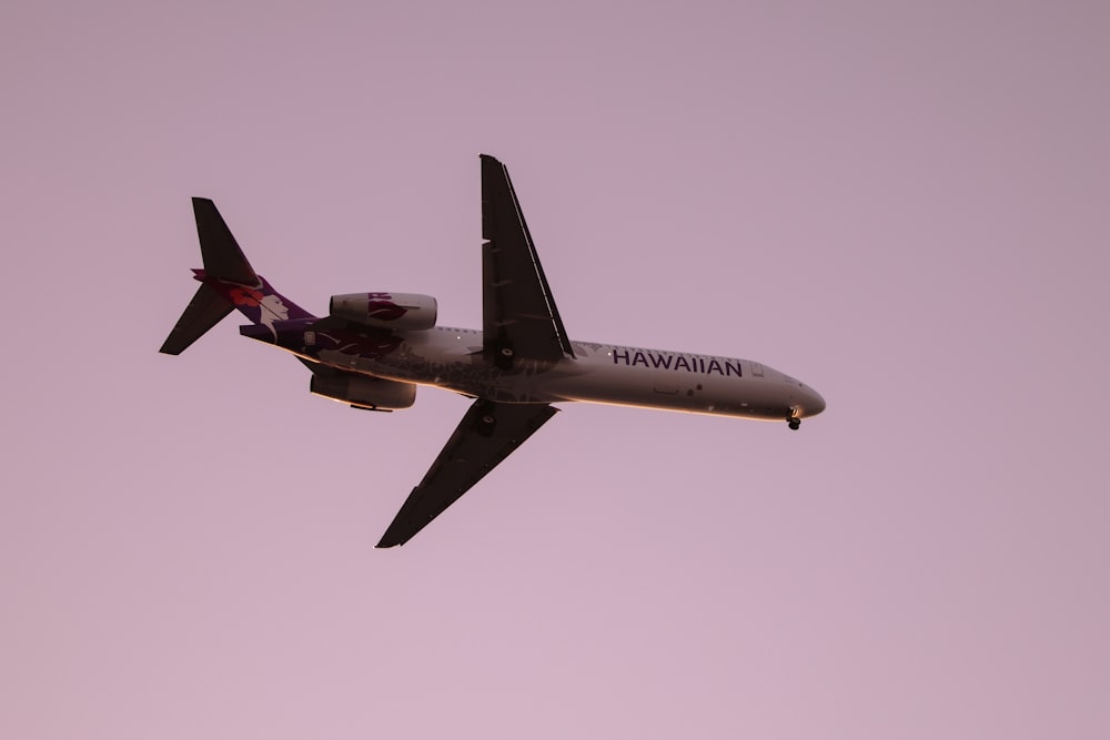 an airplane flying in the air with a pink sky background