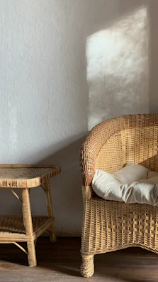 A corner nook with a rattan chair, cream cushions, and a small side table holding a candle.