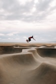 Dynamic photo of a skateboarder performing tricks near the ocean with the city skyline in the background.