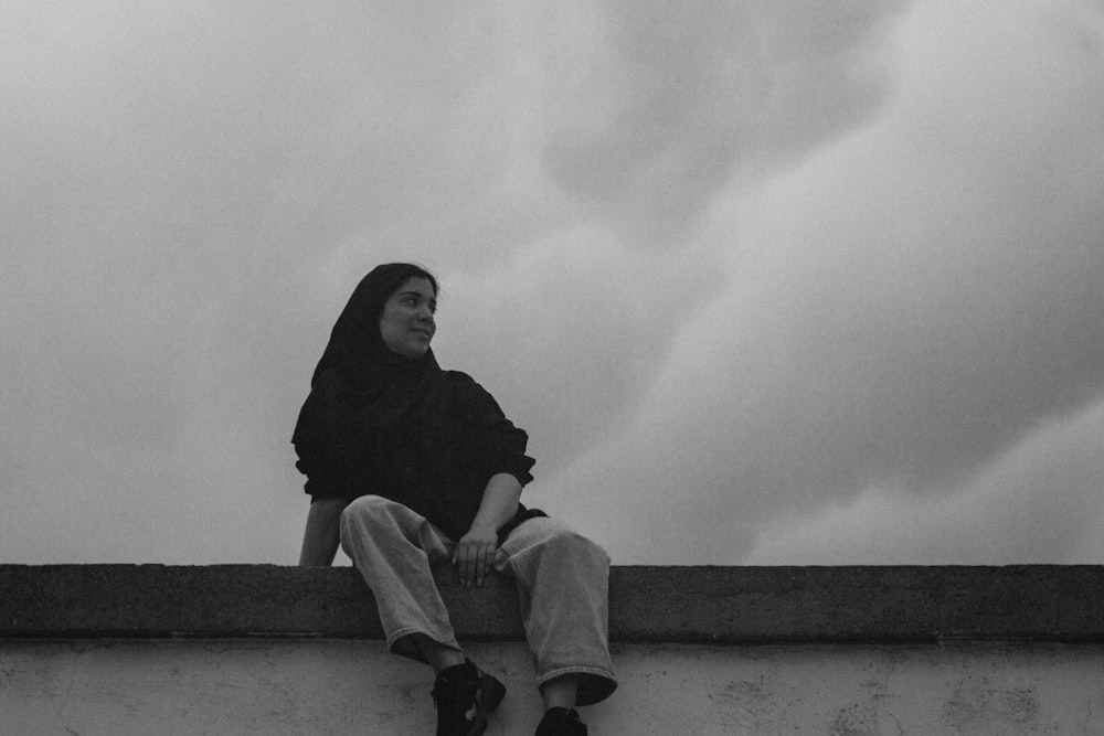 a woman sitting on top of a cement wall