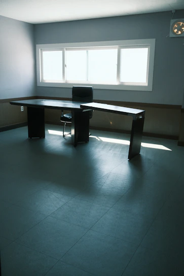 A sleek L-shaped desk in a bright home office with natural light streaming through a nearby window.
