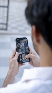 A person holds a smartphone with two hands, browsing through a gallery of images on the screen. The background is blurred, focusing attention on the phone.
