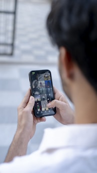 A person holds a smartphone with two hands, browsing through a gallery of images on the screen. The background is blurred, focusing attention on the phone.