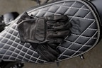 Hand-stitched motorcycle gloves displayed on a rustic wooden table.