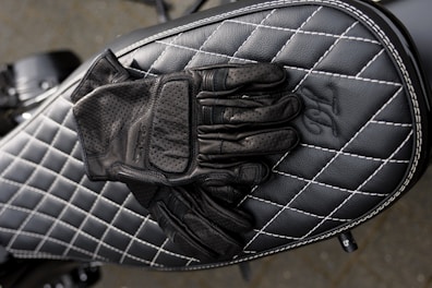 A close up of stylish Raven Rebel Moto leather gloves on a motorbike saddle
