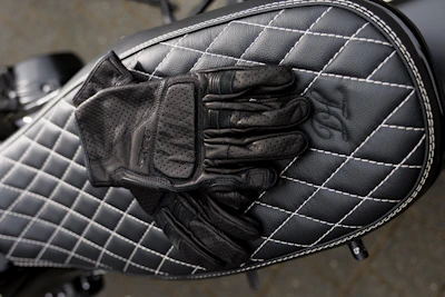 A pair of sturdy motorcycle gloves laid out on a wooden table with visible stitching details.
