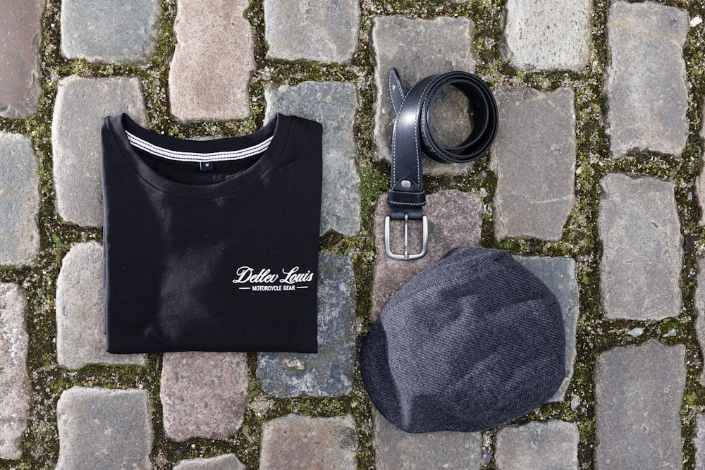 a hat, t - shirt, and belt laid out on a cobblestone