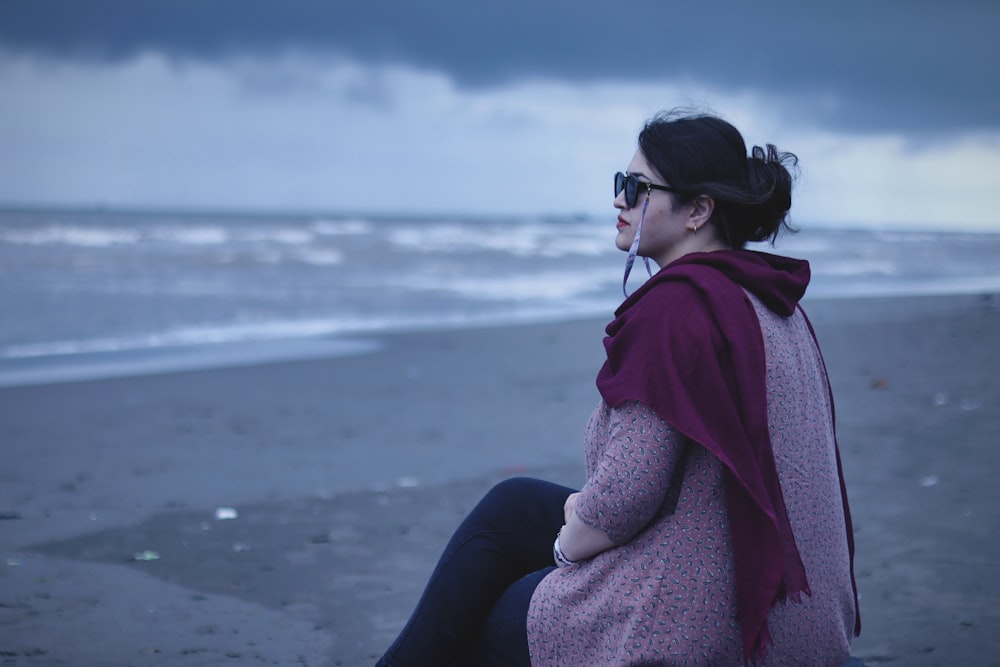 a woman sitting on the beach with her back to the camera