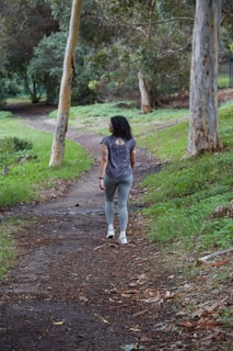 a woman is walking down a path in the woods