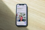 A smartphone displaying a website is placed on a wooden surface. The website features text in Polish and an image of two people standing together with indoor plants in the background.