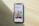 A smartphone displaying a website is placed on a wooden surface. The website features text in Polish and an image of two people standing together with indoor plants in the background.