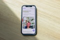A smartphone displaying a website is placed on a wooden surface. The website features text in Polish and an image of two people standing together with indoor plants in the background.