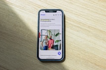 A smartphone displaying a website is placed on a wooden surface. The website features text in Polish and an image of two people standing together with indoor plants in the background.